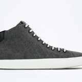 Profil latéral du mid top sneaker en toile noire et tige en cuir, fermeture à glissière interne et semelle blanche.