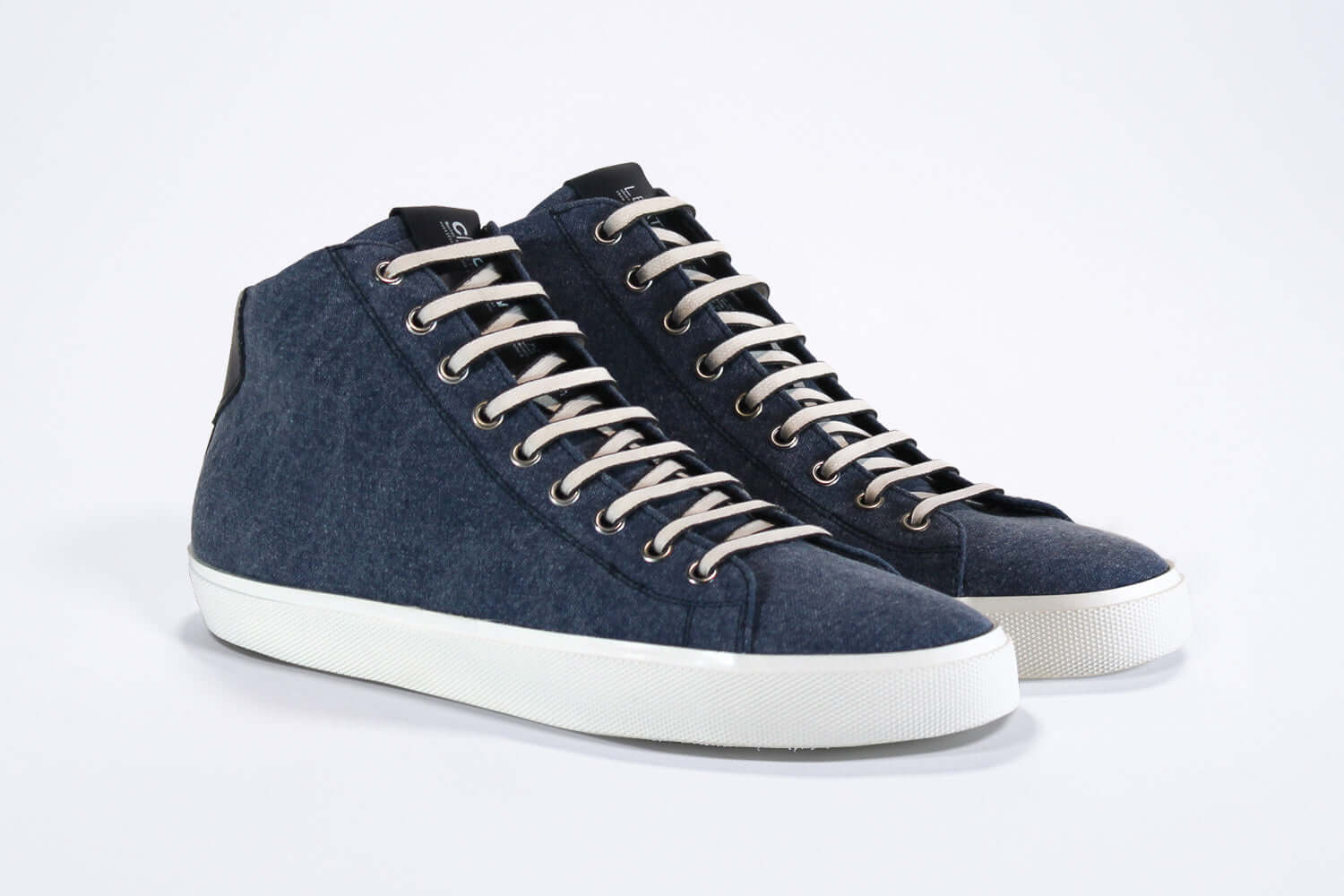 Three quarter front view of mid top sneaker in denim blue canvas and leather upper, internal zip and white sole.