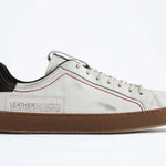 Profilo laterale di una sneaker  BASSE bianca con accenti neri. Tomaia in pelle bianca invecchiata con cuciture rosse e suola in gomma scura.
