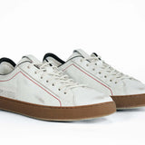 Vista frontale di tre quarti di una sneaker  BASSE bianca con accenti neri. Tomaia in pelle bianca invecchiata con cuciture rosse e suola in gomma scura.