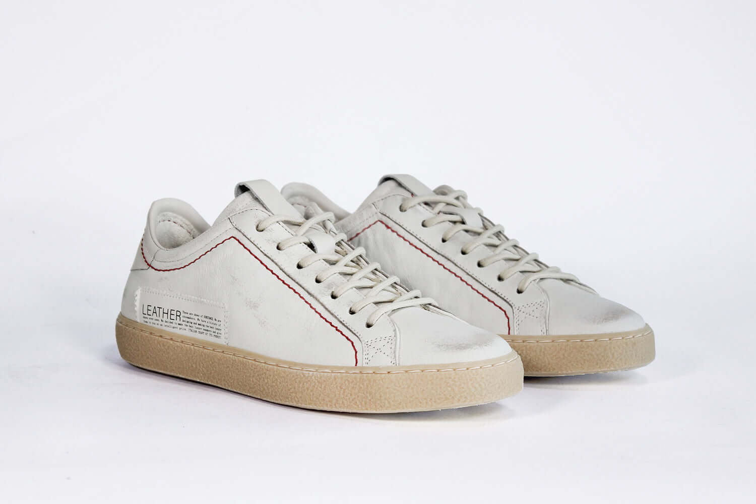 Vista frontale di tre quarti di una sneaker BASSE bianca. Tomaia in pelle bianca invecchiata con cuciture rosse e suola in gomma naturale.