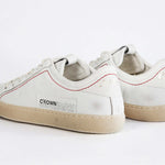 Vista posteriore della sneaker BASSE bianca. Tomaia in pelle bianca invecchiata con cuciture rosse e suola in gomma naturale.