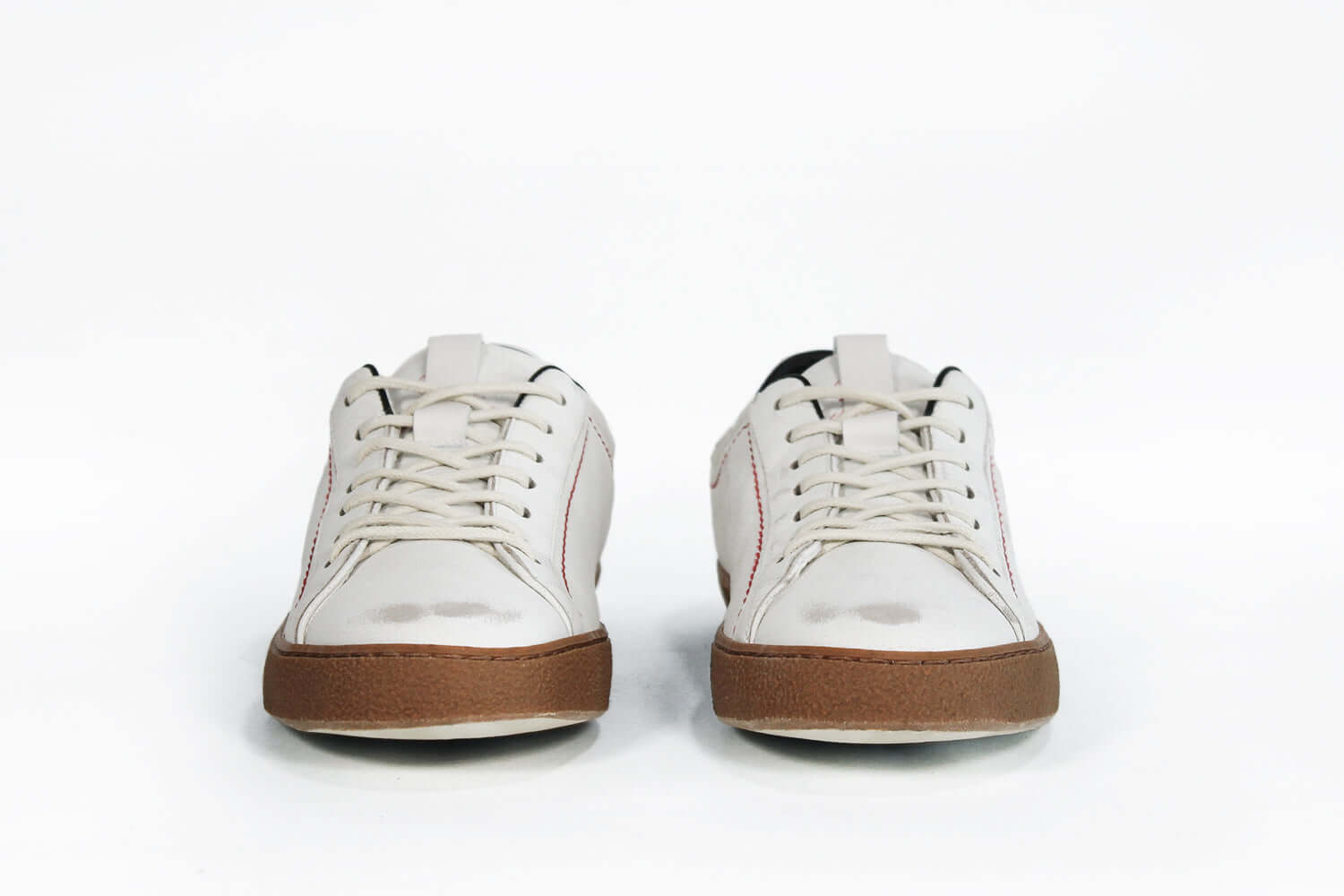 Vista frontale della sneaker  BASSE bianca con accenti neri. Tomaia in pelle bianca invecchiata con cuciture rosse e suola in gomma scura.