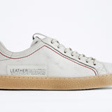 Profilo laterale della sneaker BASSE bianca. Tomaia in pelle bianca invecchiata con cuciture rosse e suola in gomma naturale.