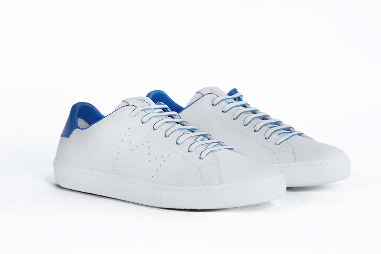 Three quarter front view of low top white sneaker with blue detailing and perforated crown logo on upper. Full leather upper and white rubber sole.