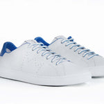 Three quarter front view of low top white sneaker with blue detailing and perforated crown logo on upper. Full leather upper and white rubber sole.