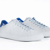 Three quarter front view of low top white sneaker with blue detailing and perforated crown logo on upper. Full leather upper and white rubber sole.