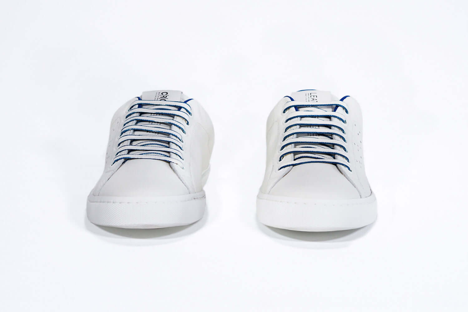 Front view of low top white sneaker with blue detailing and perforated crown logo on upper. Full leather upper and white rubber sole.