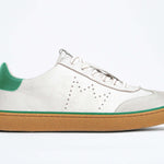 Side view of low top retro sneaker in distressed white leather with green detailing and honey coloured recycled rubber sole.