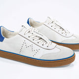 Three quarter front view of low top retro sneaker in distressed white leather with blue detailing and honey coloured recycled rubber sole.