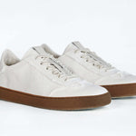 Dreiviertelansicht der Vorderseite eines sneaker aus weißem Canvas mit honigfarbener Sohle aus recyceltem Gummi.