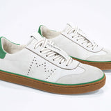 Three quarter front view of low top retro sneaker in distressed white leather with green detailing and honey coloured recycled rubber sole.