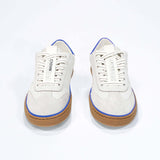 Front view of low top retro sneaker in distressed white leather with blue detailing and honey coloured recycled rubber sole.