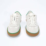 Front view of low top retro sneaker in distressed white leather with green detailing and honey coloured recycled rubber sole.