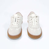 Front view of low top retro sneaker in distressed white leather with peach detailing and honey coloured recycled rubber sole.