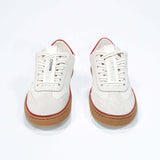 Front view of low top retro sneaker in distressed white leather with red detailing and honey coloured recycled rubber sole.