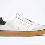 Side view of low top retro sneaker in distressed white leather with black detailing and honey coloured recycled rubber sole.