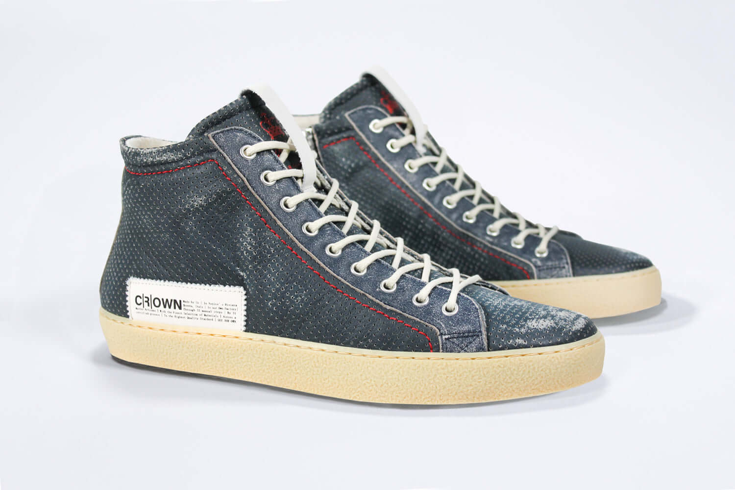 Three quarter front view of high top perforated aged navy leather sneaker with signature red stitching and a pale natural rubber sole.