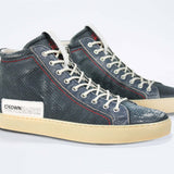 Three quarter front view of high top perforated aged navy leather sneaker with signature red stitching and a pale natural rubber sole.