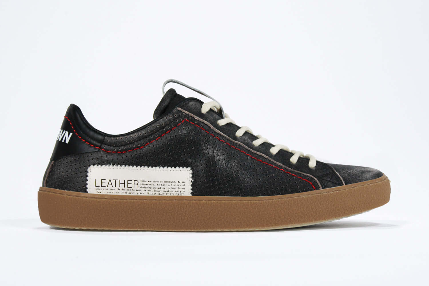 Side profile of low top black sneaker. Perforated aged black leather upper with red stitching and dark rubber sole.
