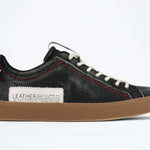 Side profile of low top black sneaker. Perforated aged black leather upper with red stitching and dark rubber sole.