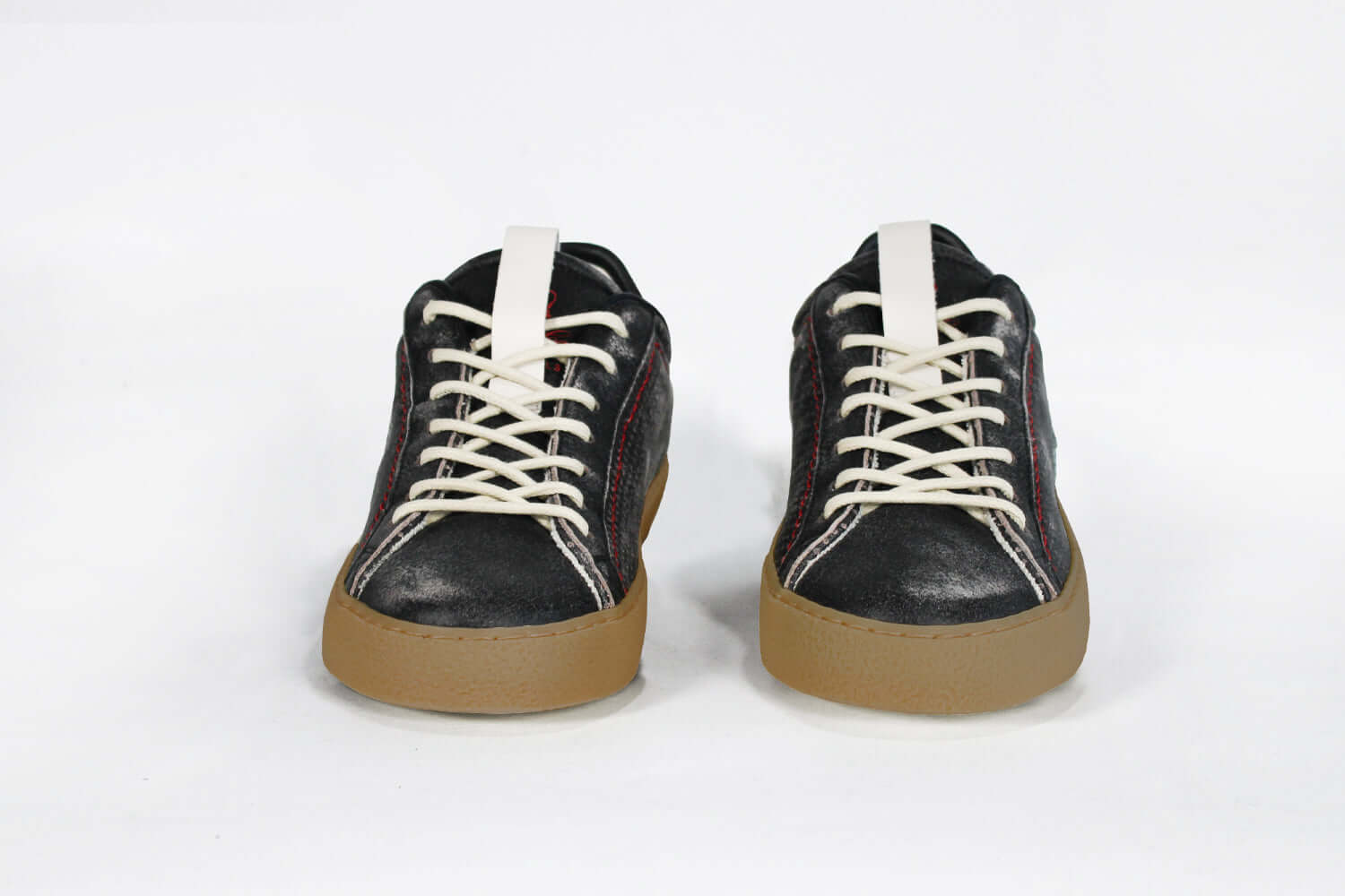 Front view of low top black sneaker. Perforated aged black leather upper with red stitching and dark rubber sole.