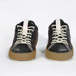 Front view of low top black sneaker. Perforated aged black leather upper with red stitching and dark rubber sole.