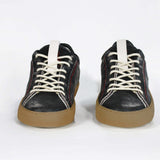 Front view of low top black sneaker. Perforated aged black leather upper with red stitching and dark rubber sole.