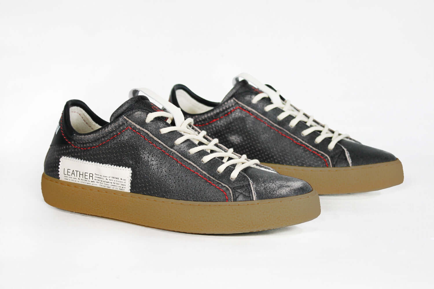 Three quarter front view of low top black sneaker. Perforated aged black leather upper with red stitching and dark rubber sole.