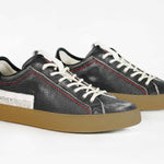 Three quarter front view of low top black sneaker. Perforated aged black leather upper with red stitching and dark rubber sole.