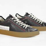 Three quarter front view of low top black sneaker. Perforated aged black leather upper with red stitching and dark rubber sole.