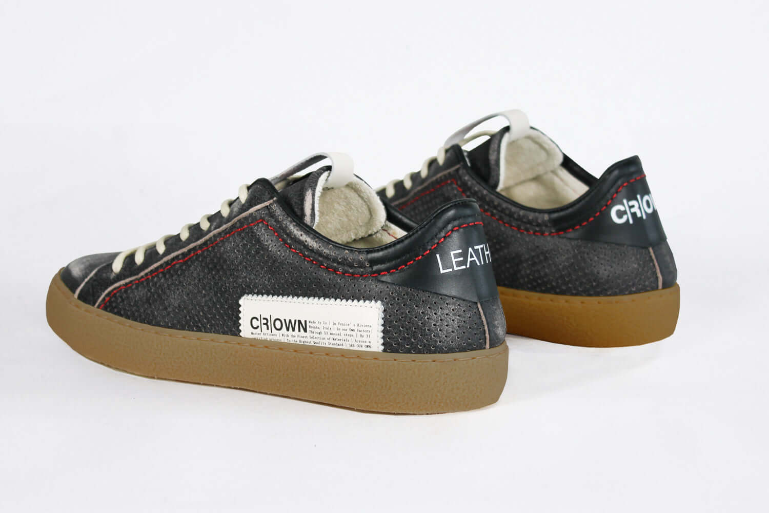 Back view of low top black sneaker. Perforated aged black leather upper with red stitching and dark rubber sole.