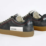 Back view of low top black sneaker. Perforated aged black leather upper with red stitching and dark rubber sole.