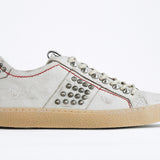 Side profile of low top white studded sneaker. Aged white leather upper with silver studs and natural rubber sole.