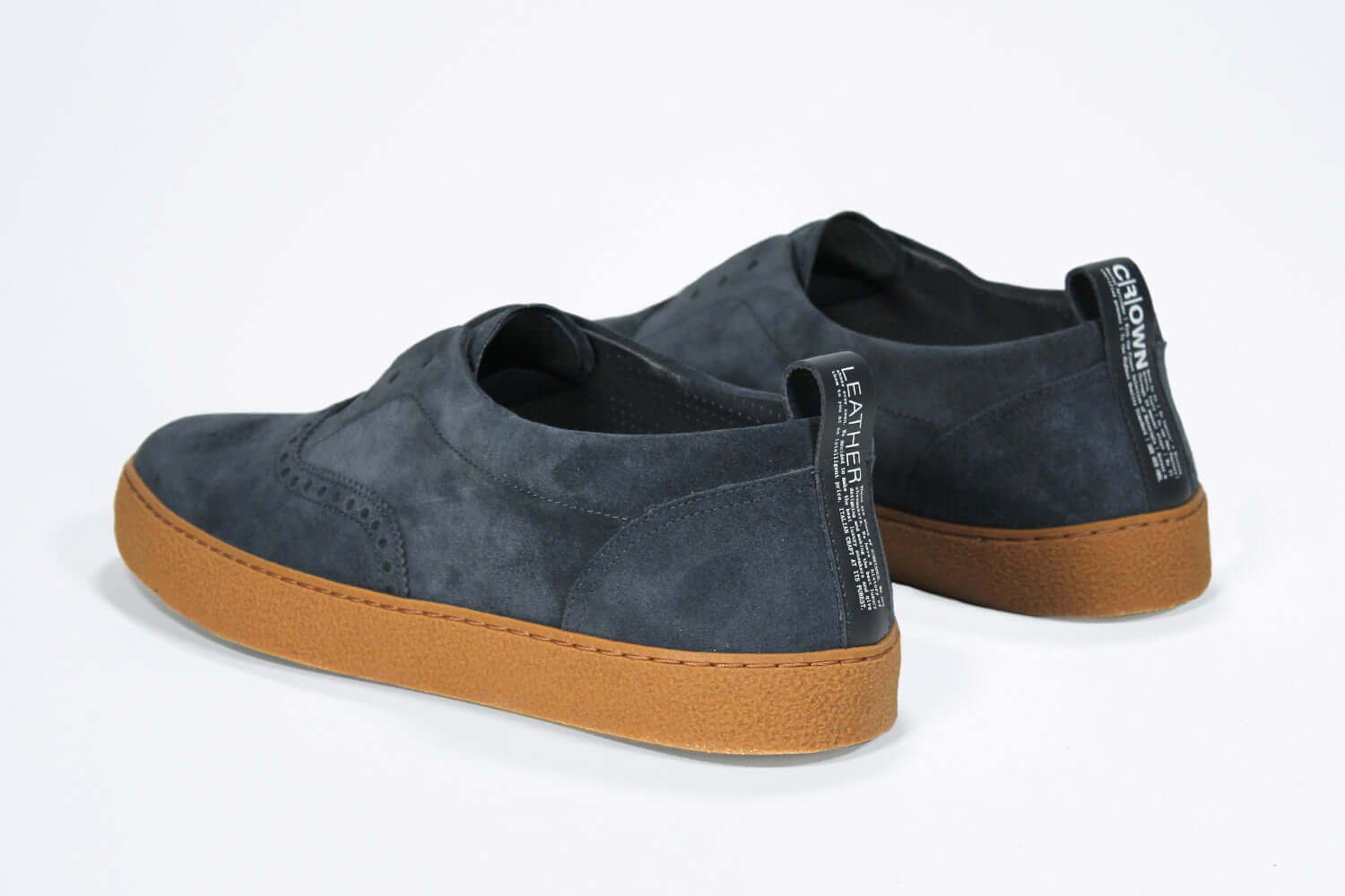 Back view of loafer style sneaker. Navy suede upper with perforated crown logo, elasticated tongue and a honey coloured recycled rubber sole.