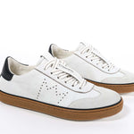 Three quarter view of low top retro sneaker in distressed white leather with black detailing and honey coloured recycled rubber sole.