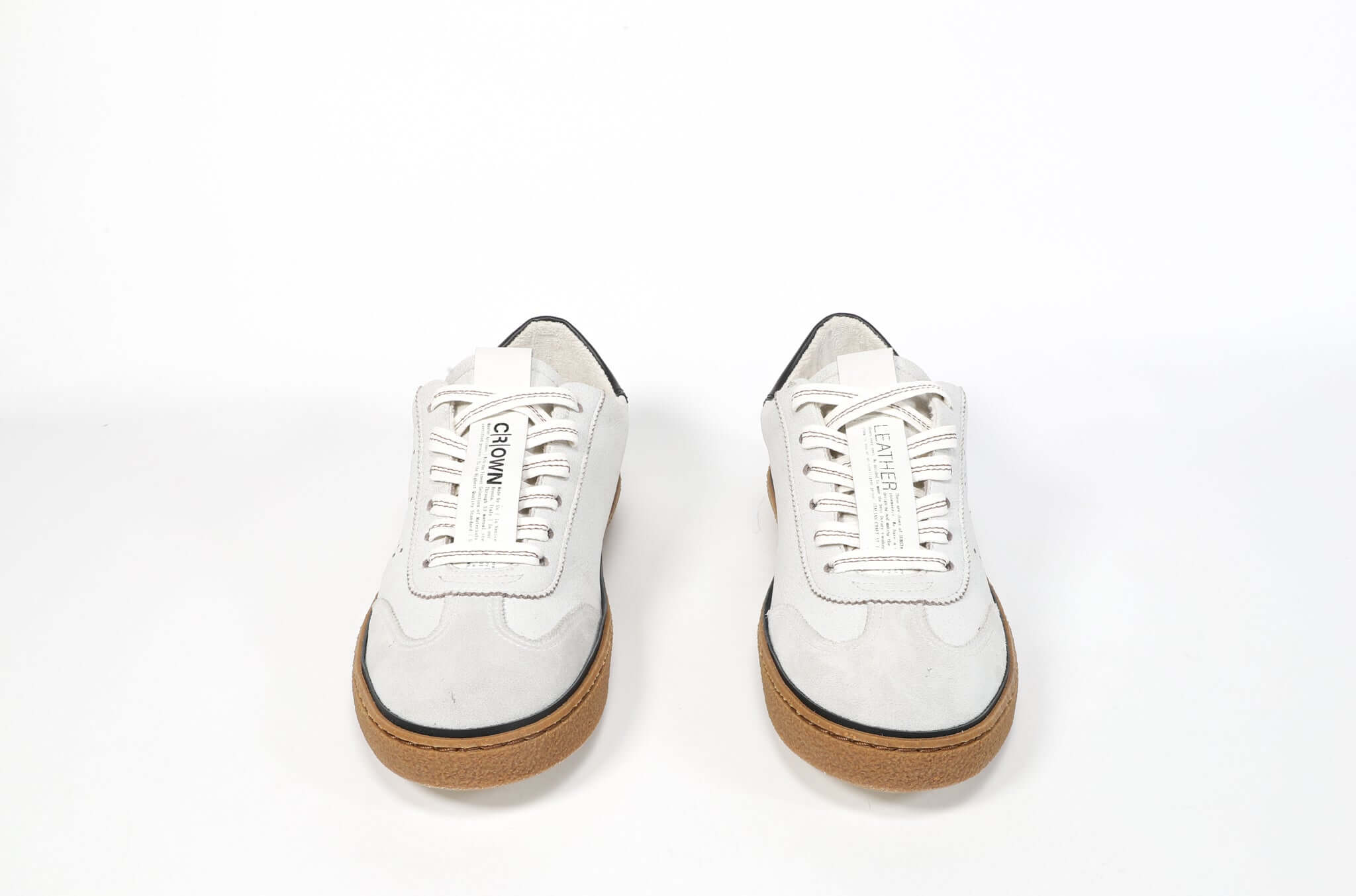 Front view of low top retro sneaker in distressed white leather with black detailing and honey coloured recycled rubber sole.