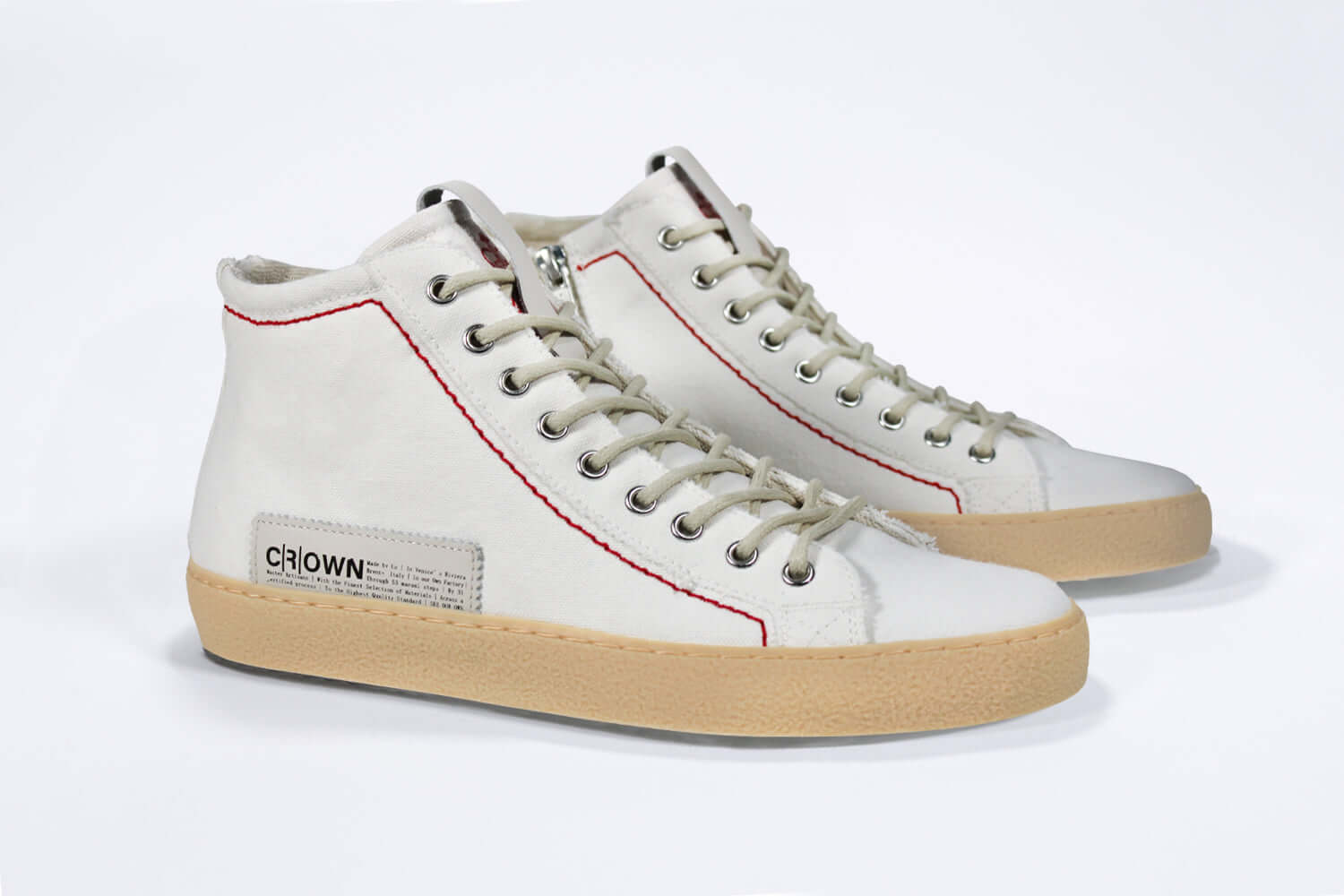 Three quarter front viewof high top canvas sneaker. White canvas upper with signature red stitching and pale natural rubber sole.