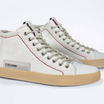 Three quarter front viewof high top canvas sneaker. White canvas upper with signature red stitching and pale natural rubber sole.