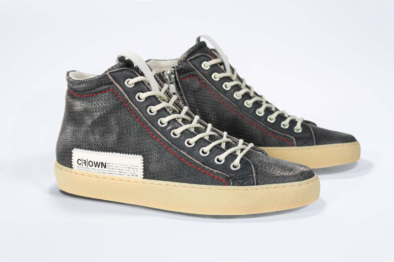 Three quarter front view of high top sneaker. Perforated distressed black leather sneakers with signature red stitching and pale natural rubber sole.
