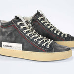 Three quarter front view of high top sneaker. Perforated distressed black leather sneakers with signature red stitching and pale natural rubber sole.