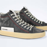 Three quarter front view of high top sneaker. Perforated distressed black leather sneakers with signature red stitching and pale natural rubber sole.