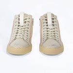 Front view of high top sneaker. Perforated milk leather sneakers with signature red stitching and pale natural rubber sole.