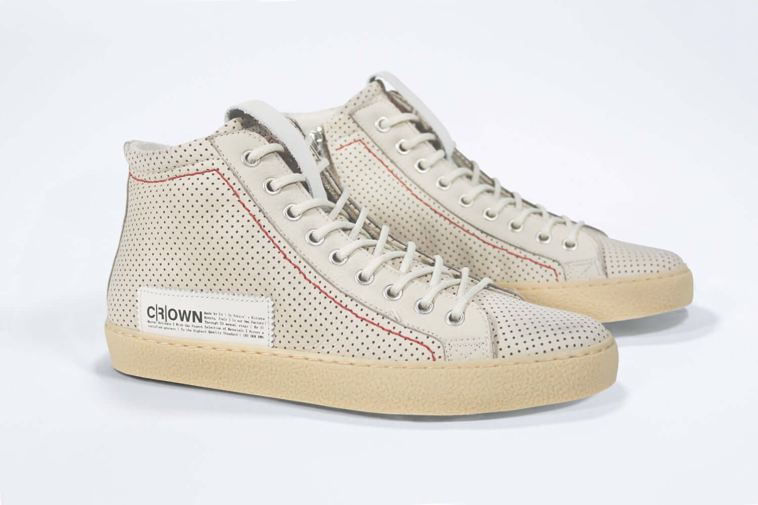 Three quarter front view of high top sneaker. Perforated milk leather sneakers with signature red stitching and pale natural rubber sole.