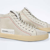 Three quarter front view of high top sneaker. Perforated milk leather sneakers with signature red stitching and pale natural rubber sole.