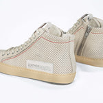 Back view of high top sneaker. Perforated milk leather sneakers with signature red stitching and pale natural rubber sole.