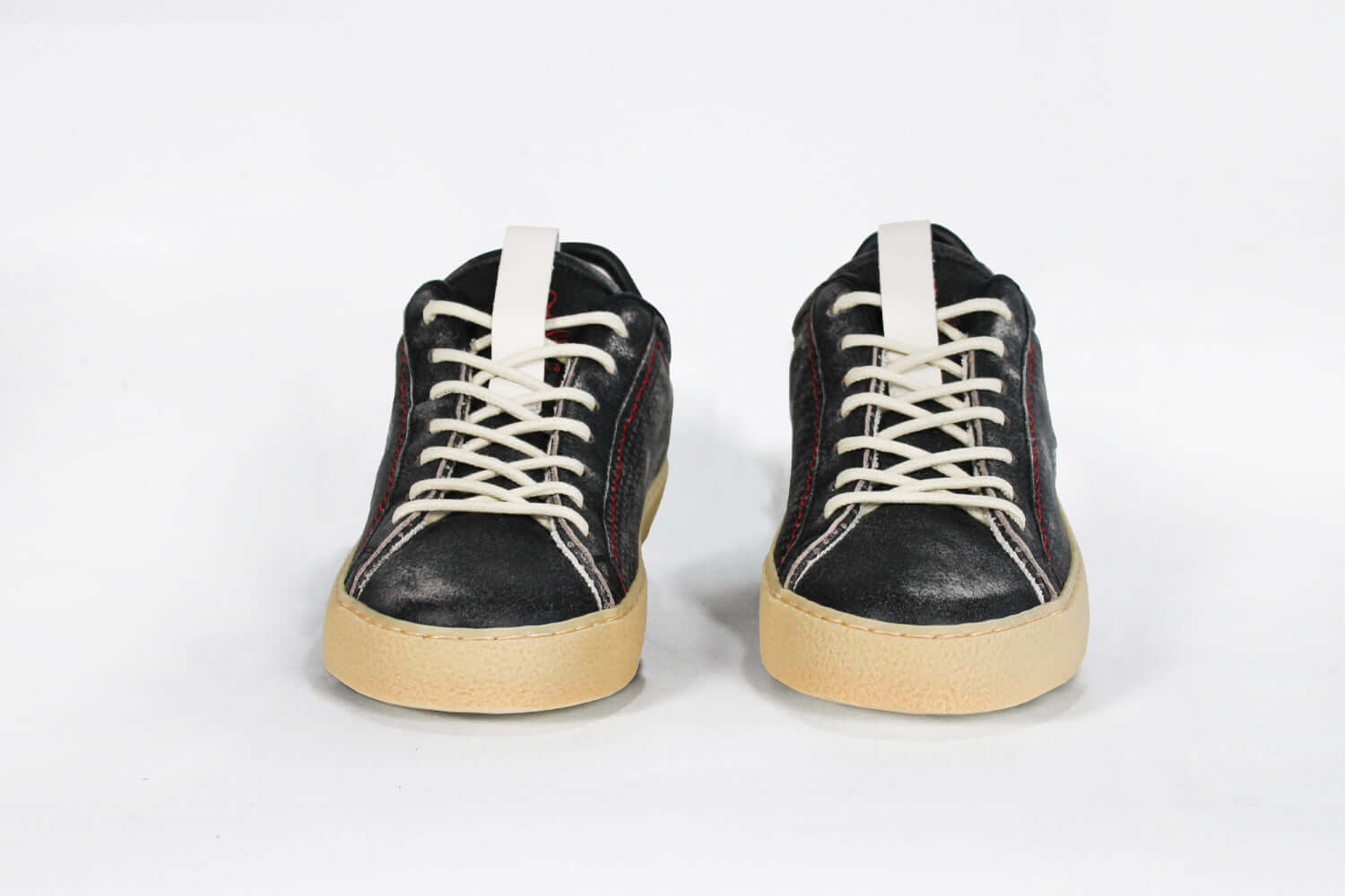 Front view of low top perforated aged black leather sneaker with red stitching detail and a pale natural rubber sole.