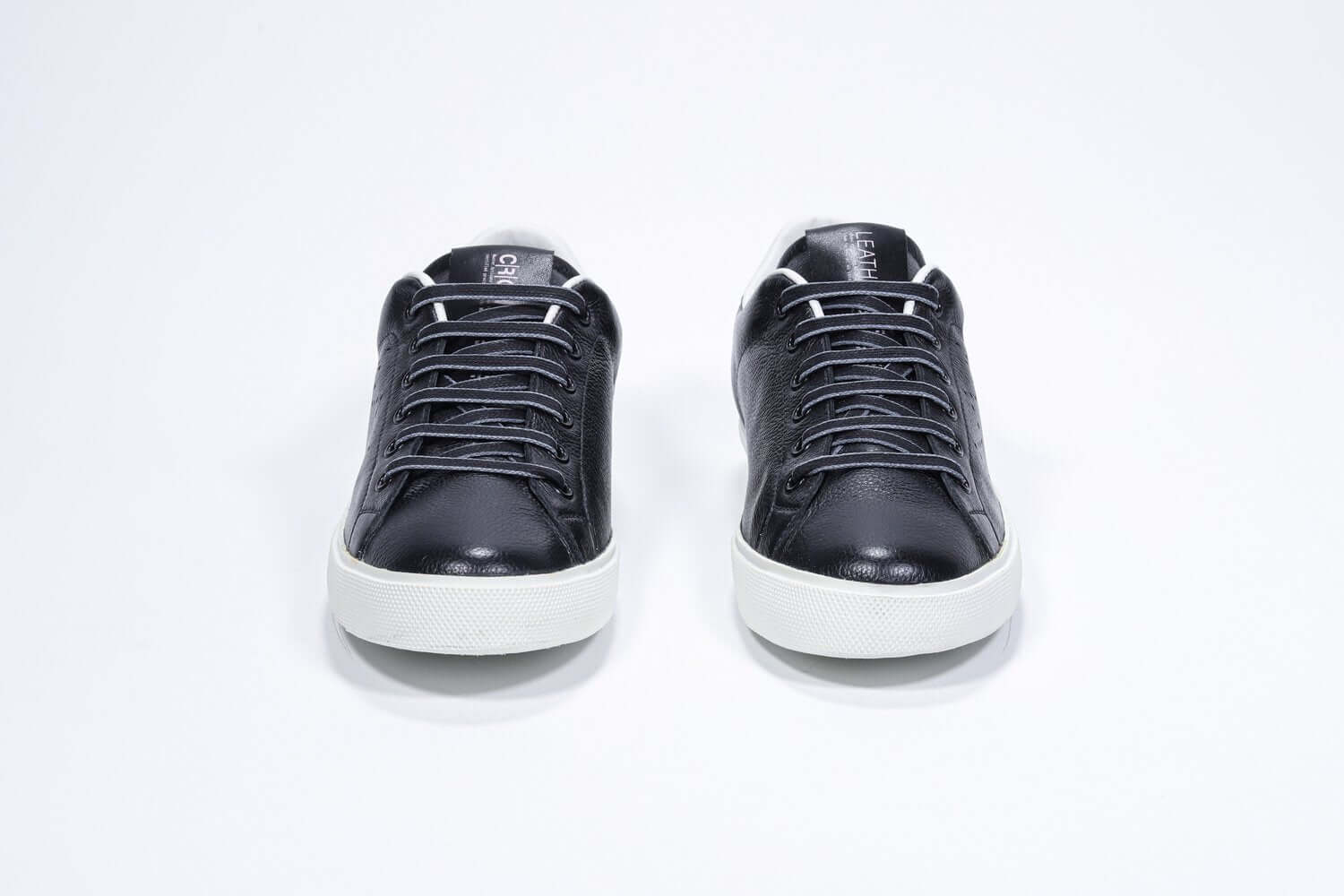 Front view of low top black sneaker with white detailing and perforated crown logo on upper. Full leather upper and white rubber sole.