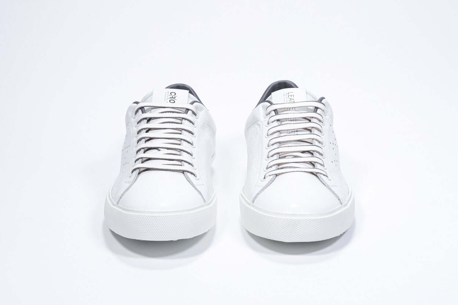 Front view of low top white sneaker with dark grey detailing and perforated crown logo on upper. Full leather upper and white rubber sole.