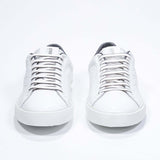 Front view of low top white sneaker with dark grey detailing and perforated crown logo on upper. Full leather upper and white rubber sole.